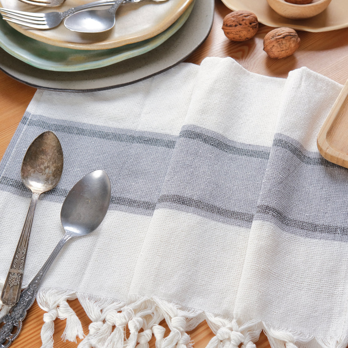 Dining table setting with a striped white and gray napkin, silverware, and wooden cutting board.
