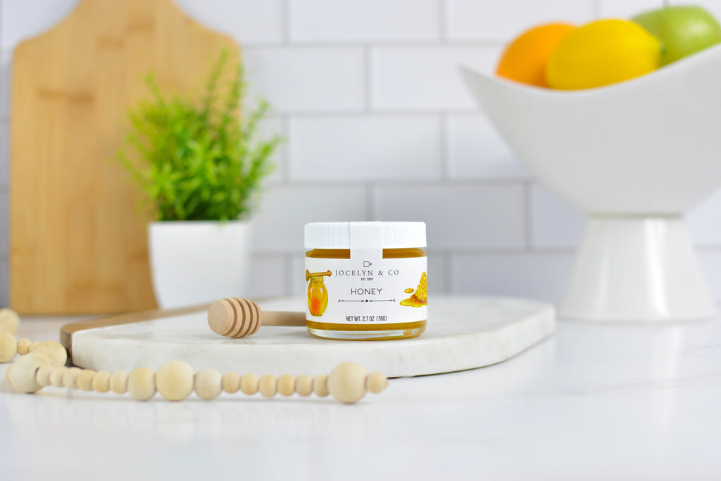 Jar of honey on a kitchen counter with fruits and a plant in the background