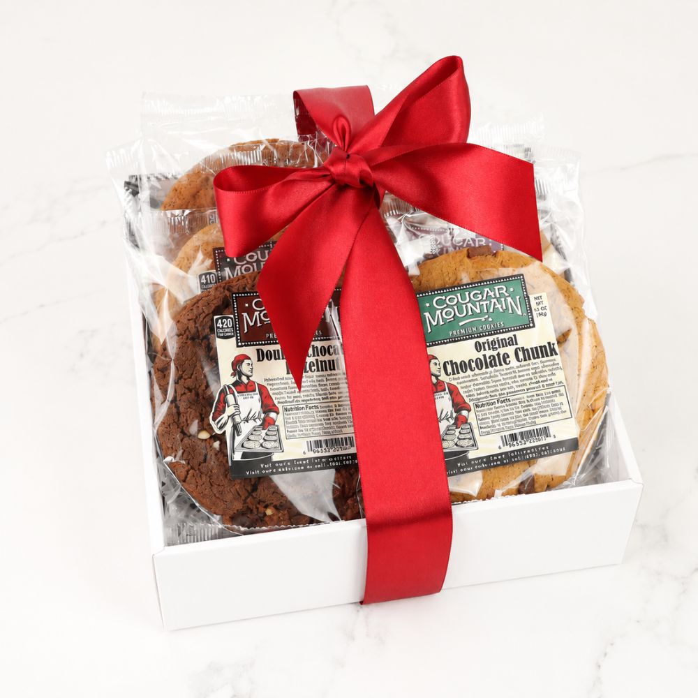 A gift box of Cougar Mountain Chocolate Chunk cookies, featuring a white box, clear plastic wrapping, a large red satin bow, and visible chocolate chip cookies inside.