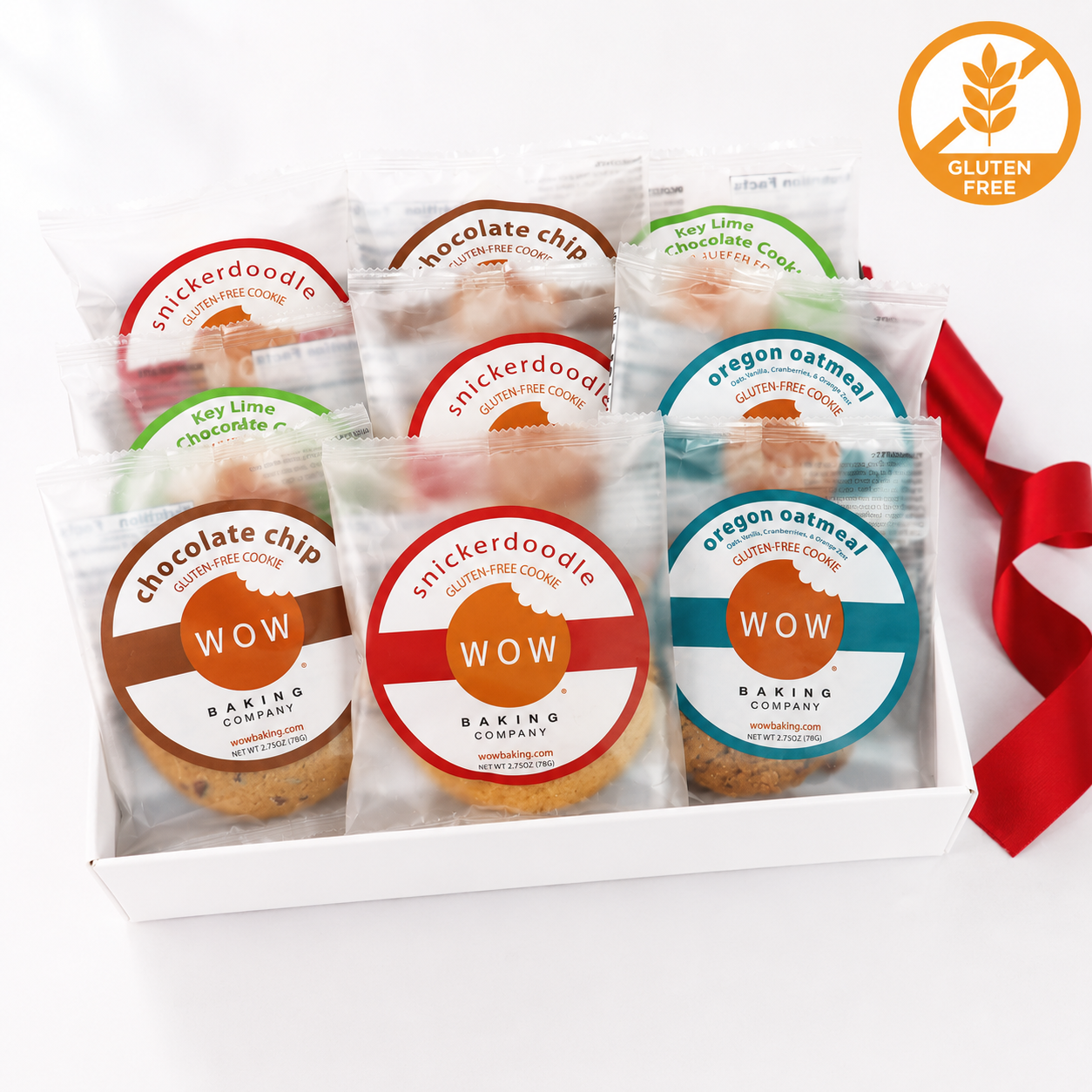 A white gift box containing six individually wrapped gluten-free cookies from Wow Baking Company, with colorful round labels showing flavors like chocolate chip, snickerdoodle, key lime chocolate cookie, soy lime chocolate cookie, and Oregon oatmeal. A red ribbon is tied to the box, and a gold 'Gluten Free' badge appears in the top right corner.